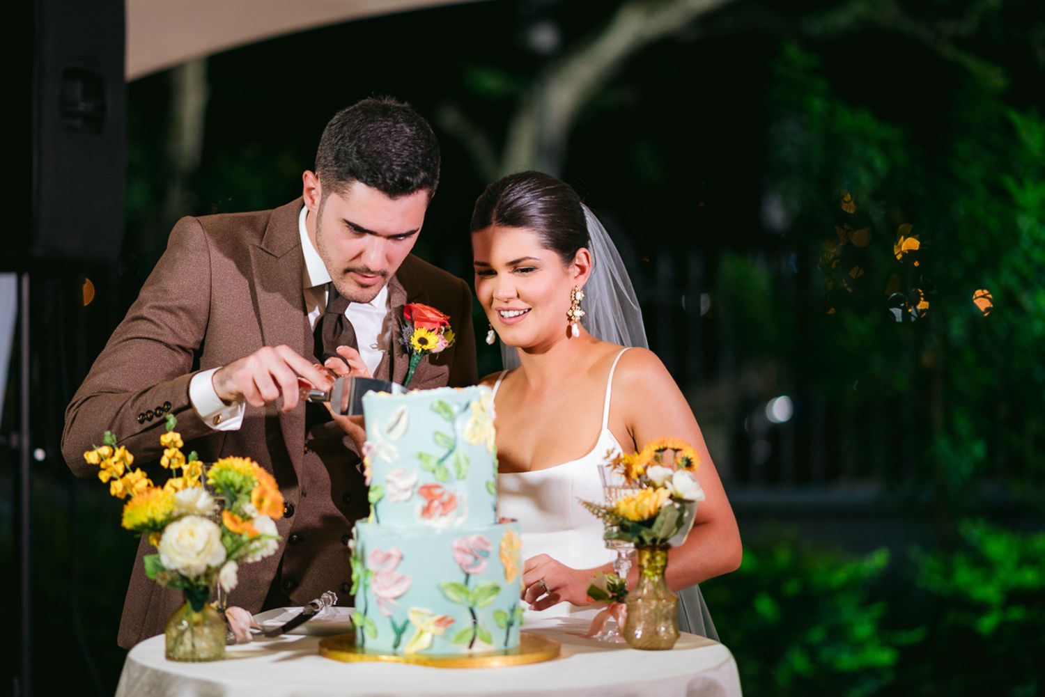 Smiling couple cut and feed each other bites of their colorful wedding cake during evening reception.