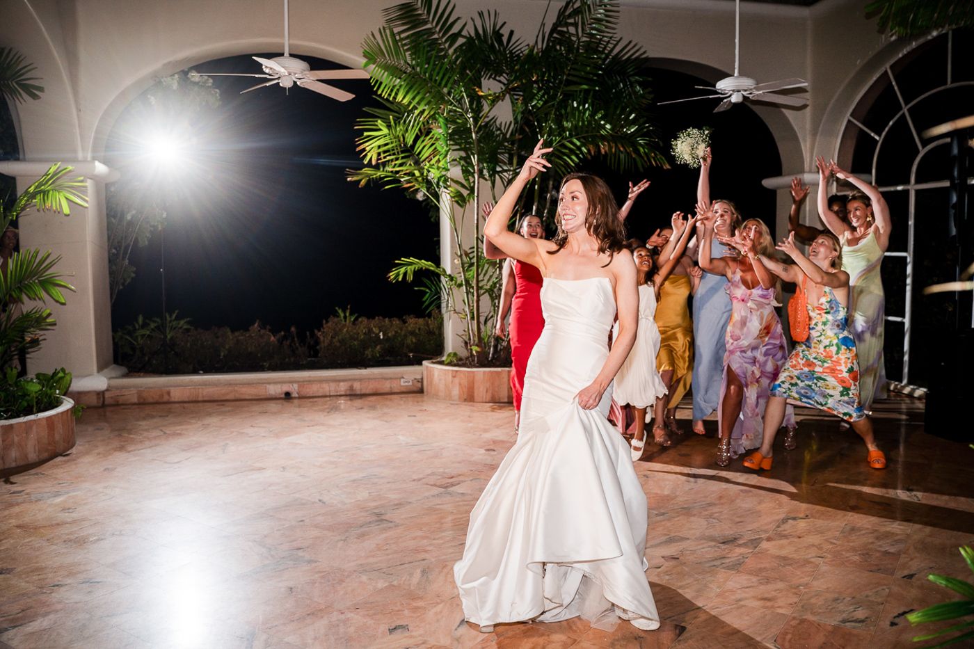 A celebratory dance moment at a wedding reception with tropical palm decor and arched windows.