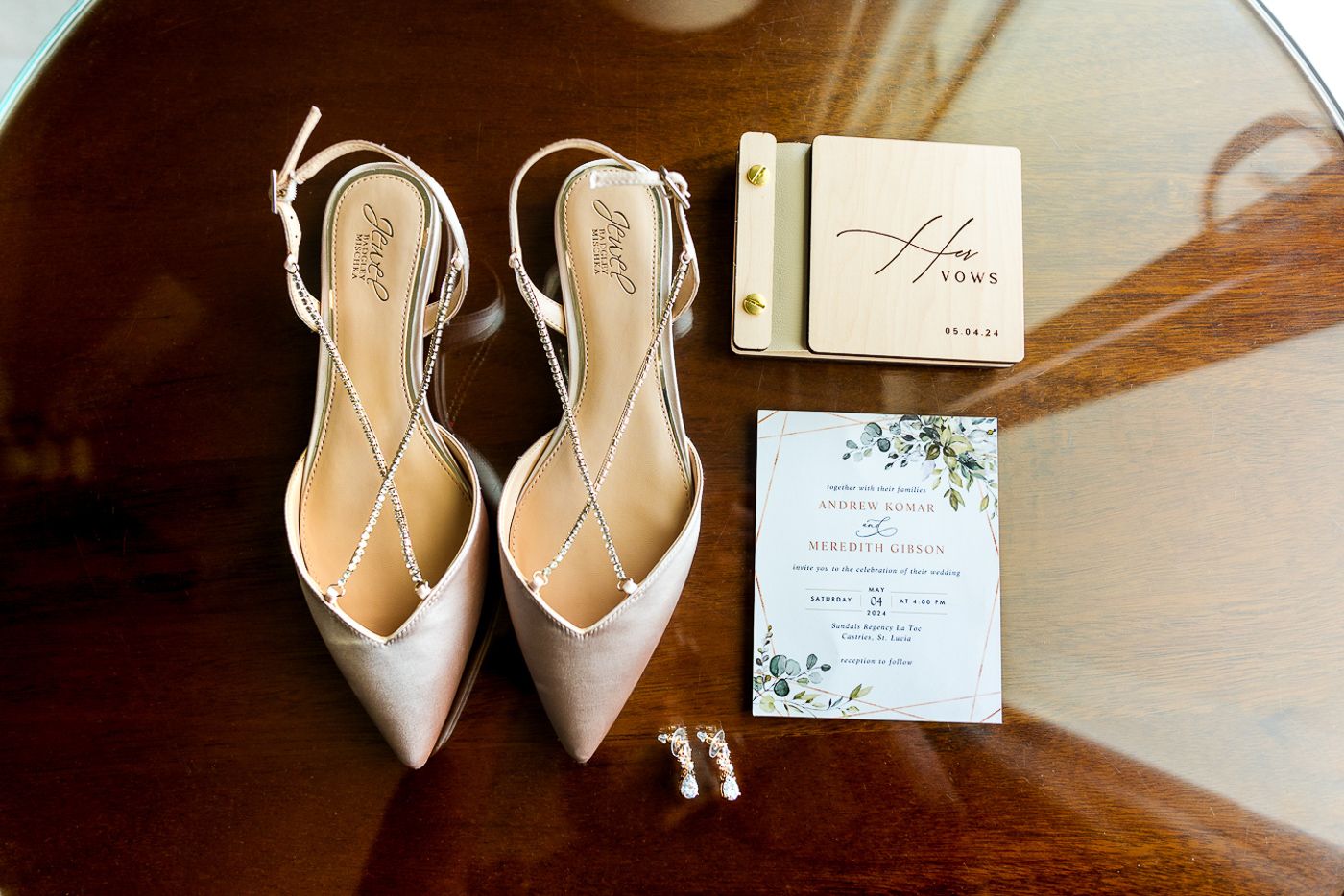 Elegant beige wedding shoes and invitation suite arranged on wooden surface.