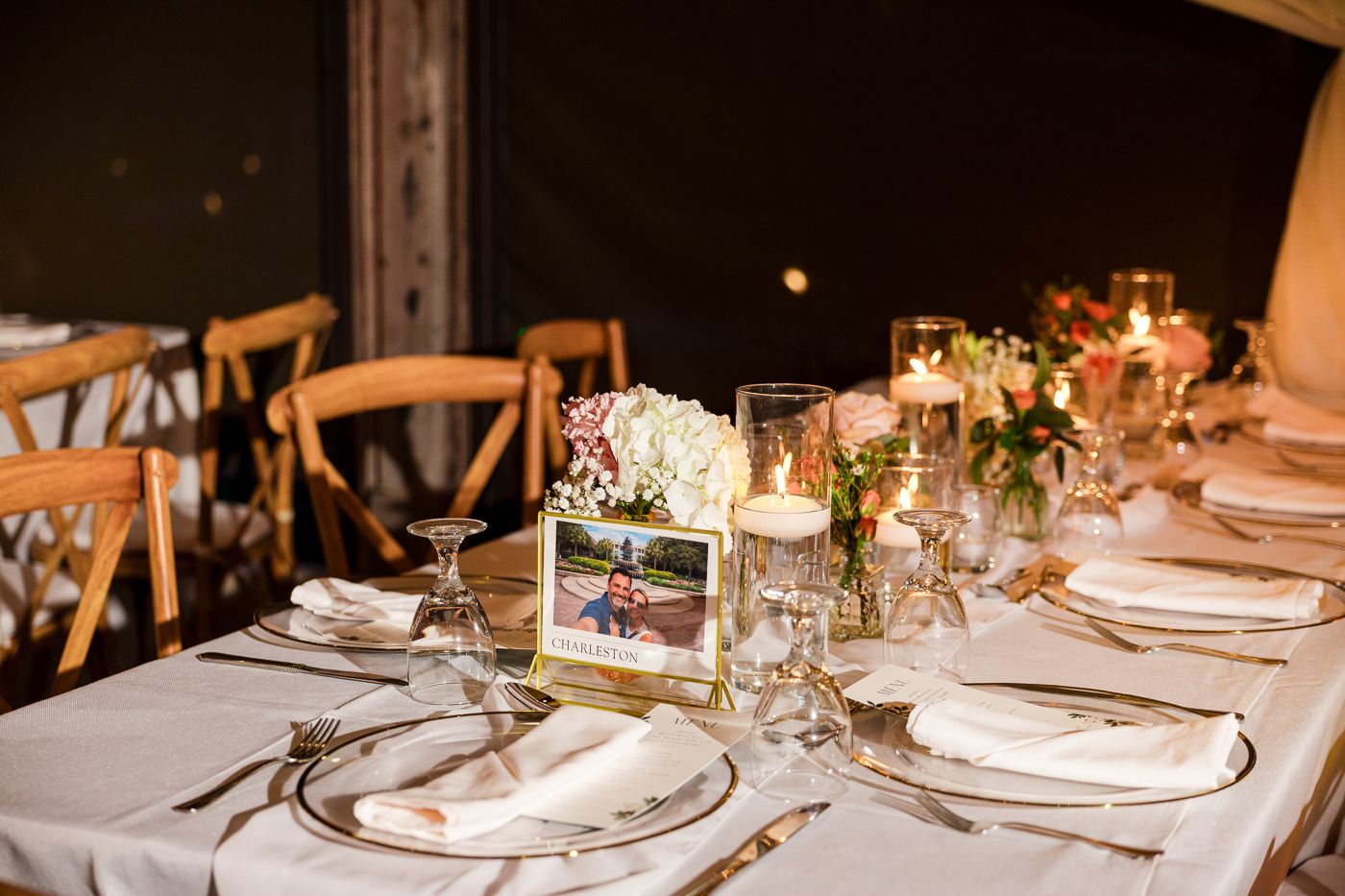 Elegant wedding reception table with white linens, floral centerpieces, candles, and a framed photo table number.
