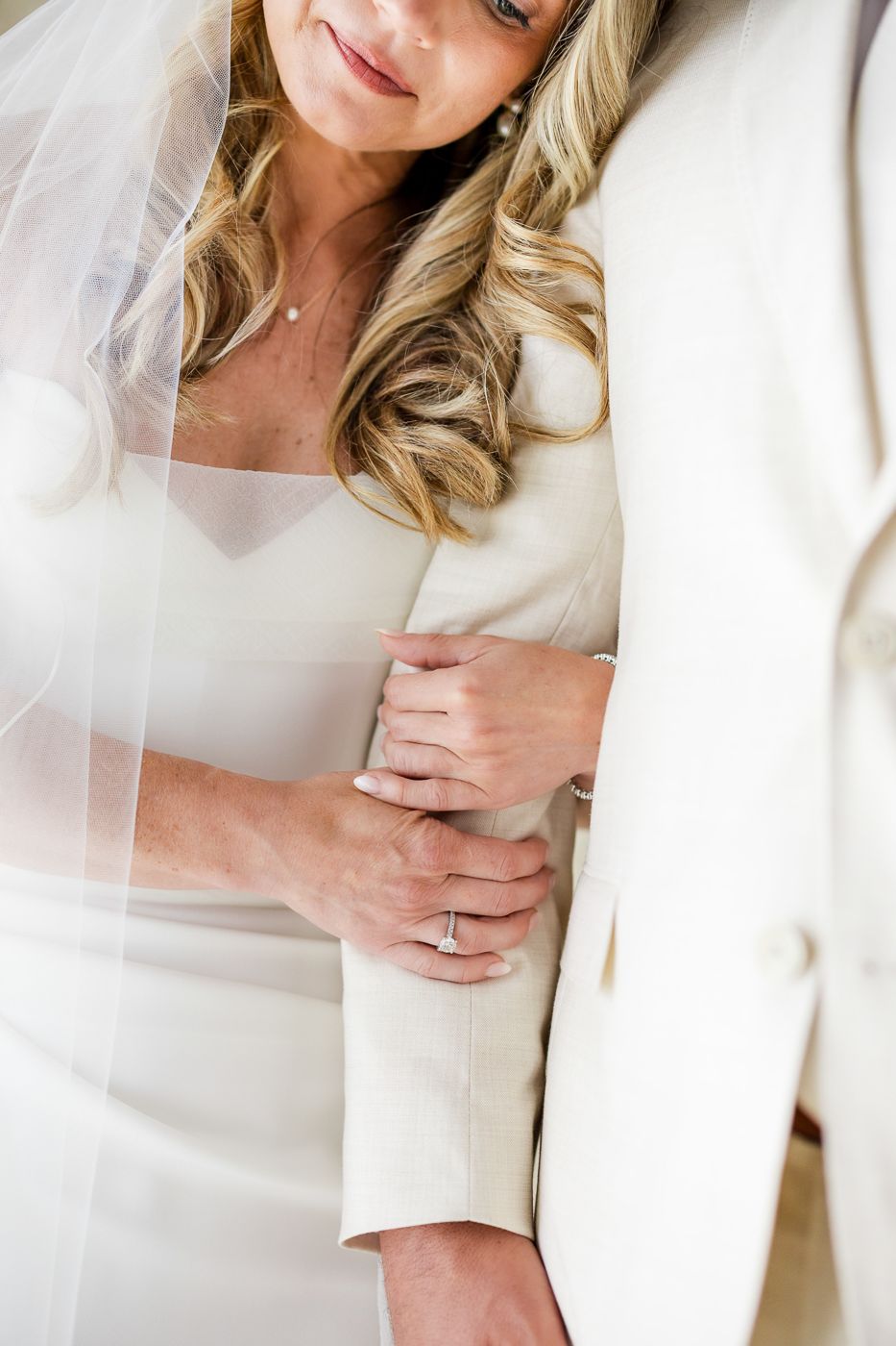 Close-up of bride in white strapless gown and veil embracing groom, showcasing her diamond engagement ring.