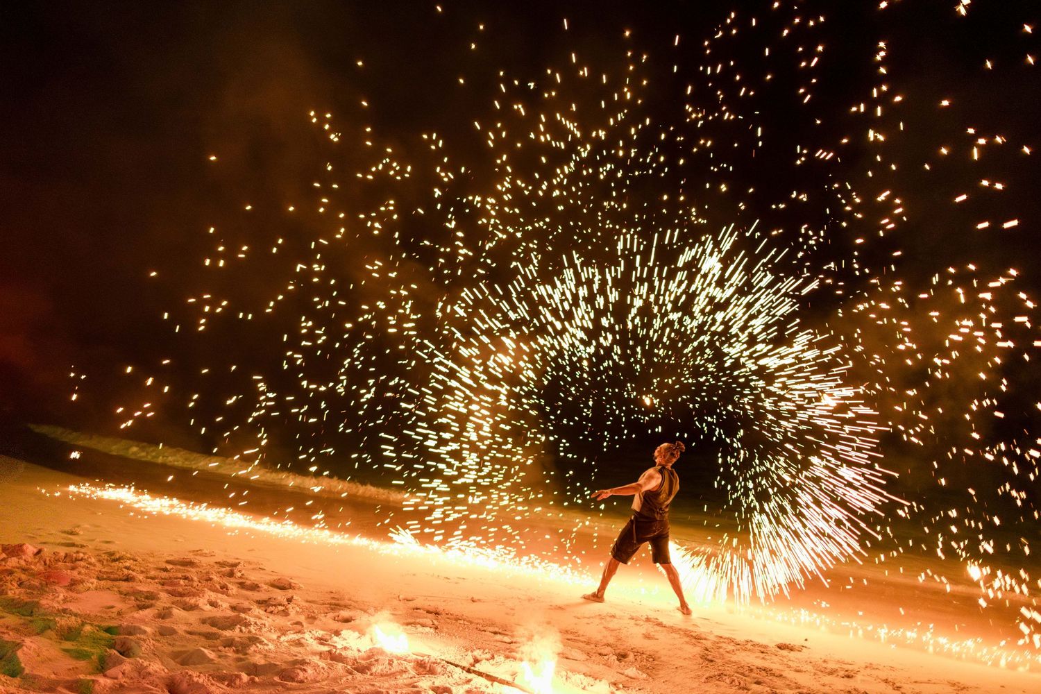 Performers spin and dance with sparking fire poi creating trails of light against a dark background at  Fairmont Barbados, Celeste and Reece
