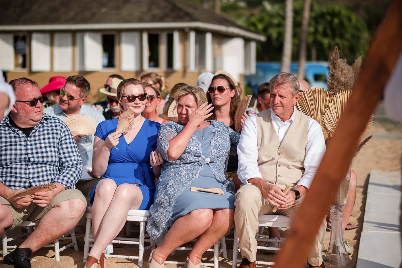 Wedding guests seated in casual attire watching a beach ceremony.