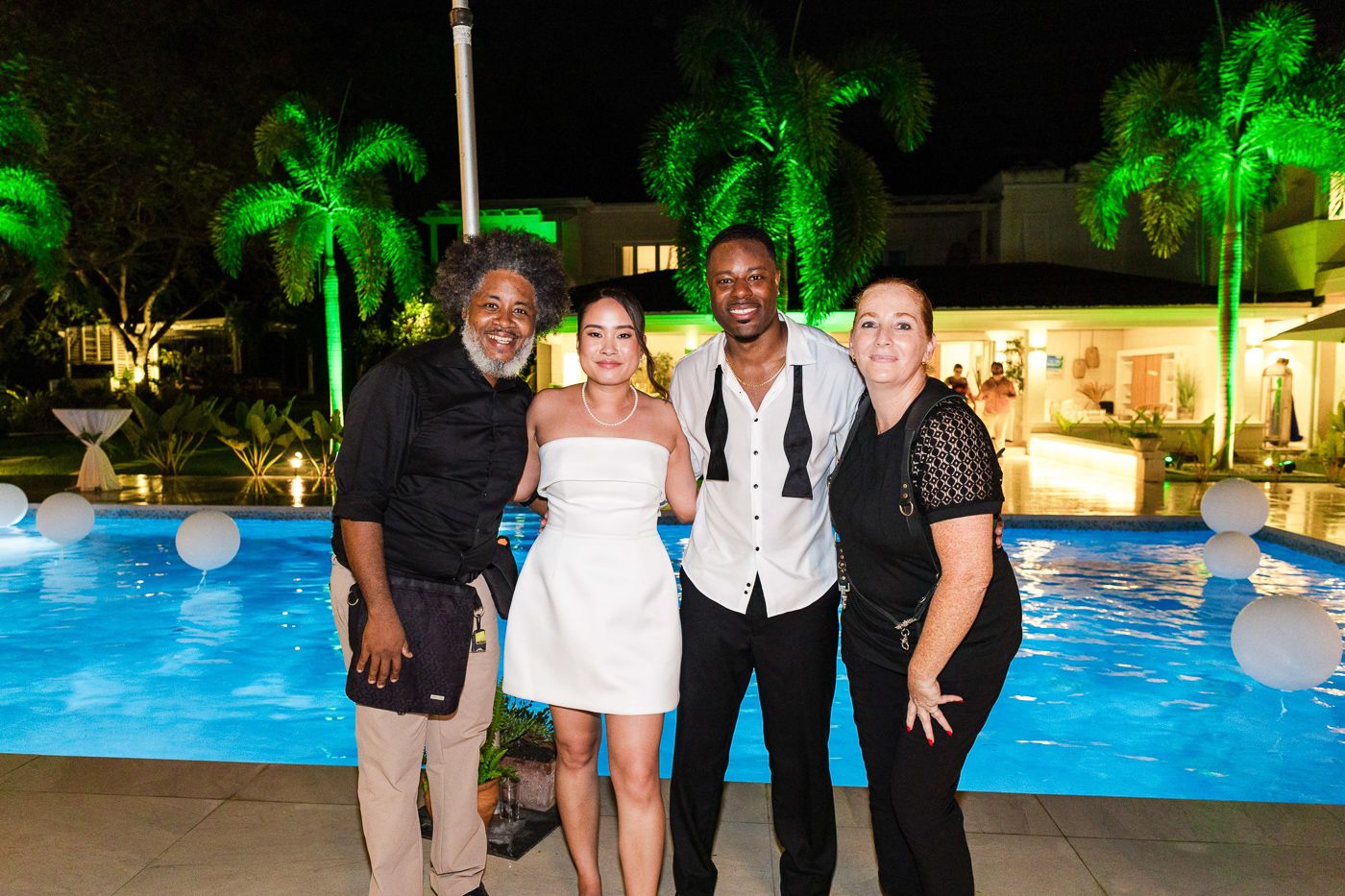 Nighttime poolside celebration with green-lit palm trees and dancing guests.