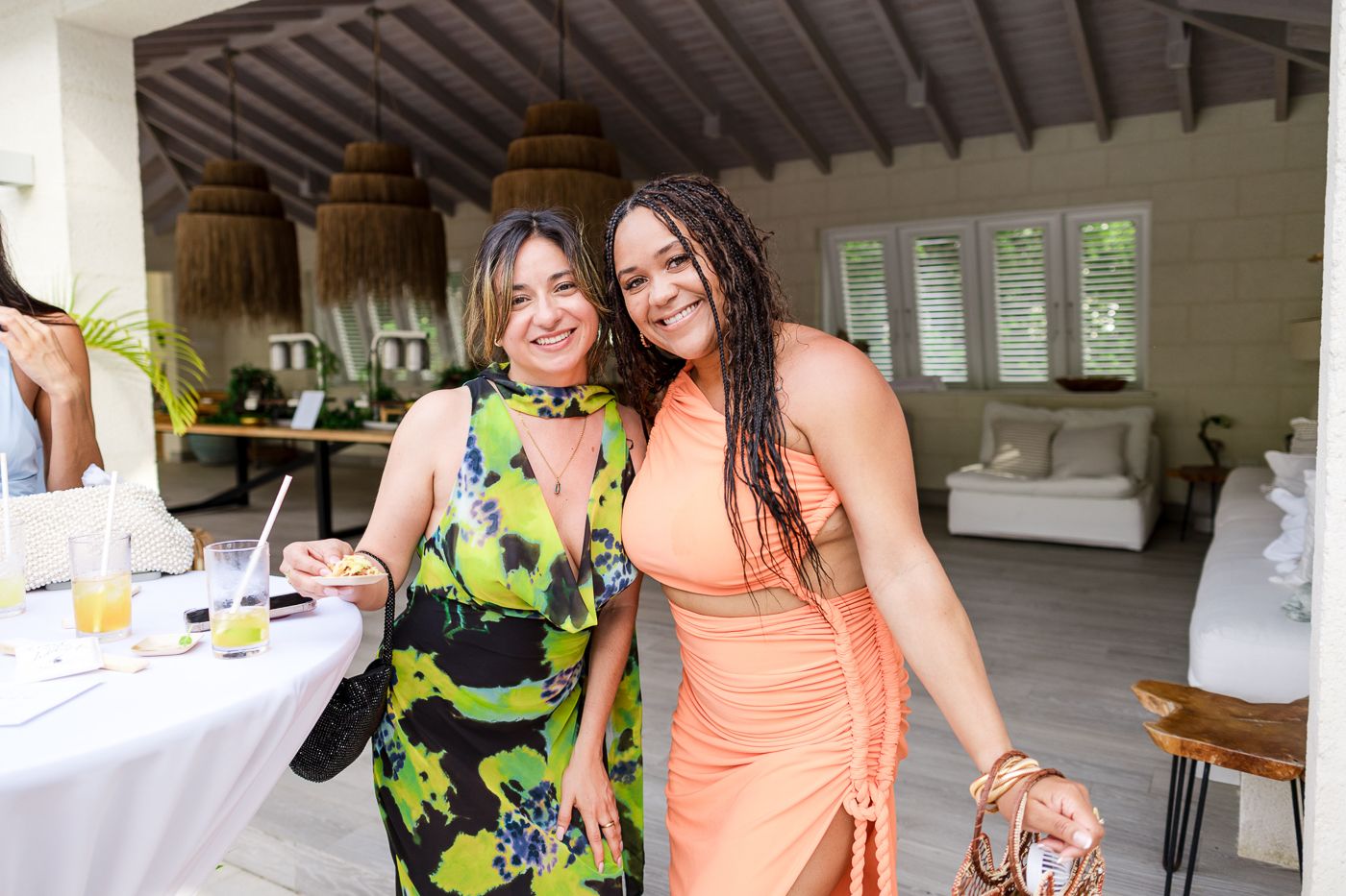 Two wedding guests in colorful dresses smile during the reception inside a rustic venue.