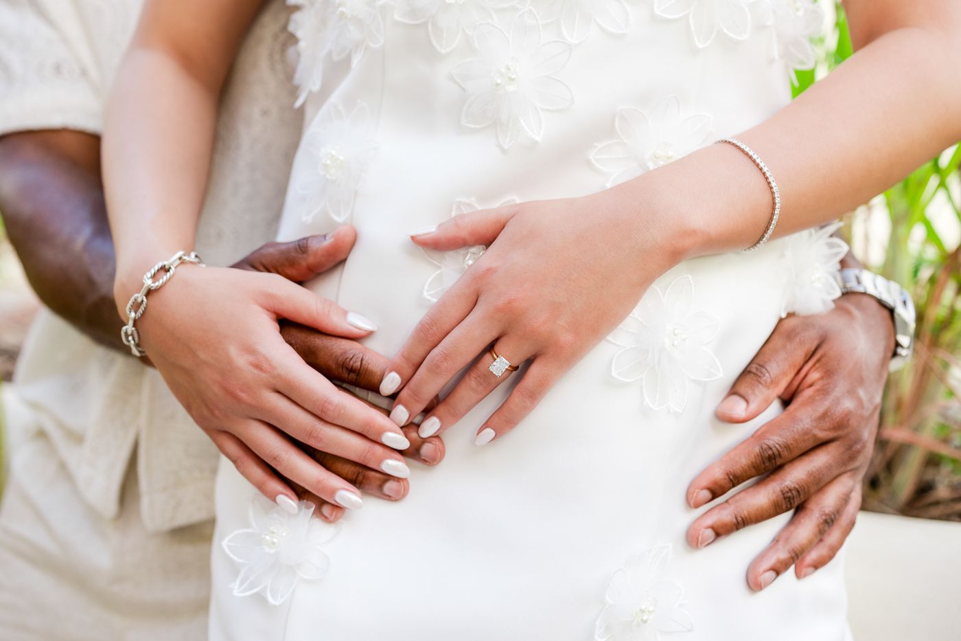 Close-up of hands wearing wedding rings against white fabric.