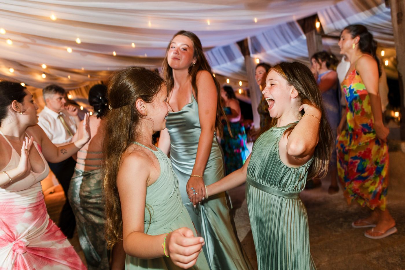 Girls in green satin dresses dancing joyfully at an elegant wedding reception celebration.