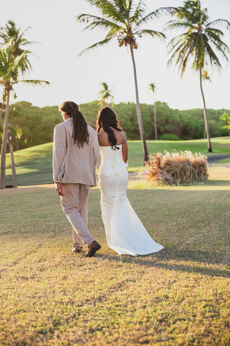 Bride and groom walking hand in hand on tropical golf course at sunset, palm trees in background.