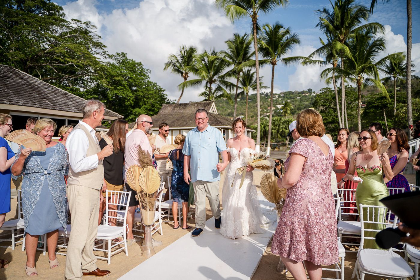 Outdoor wedding ceremony setup with white chairs and tropical palm trees under blue skies.