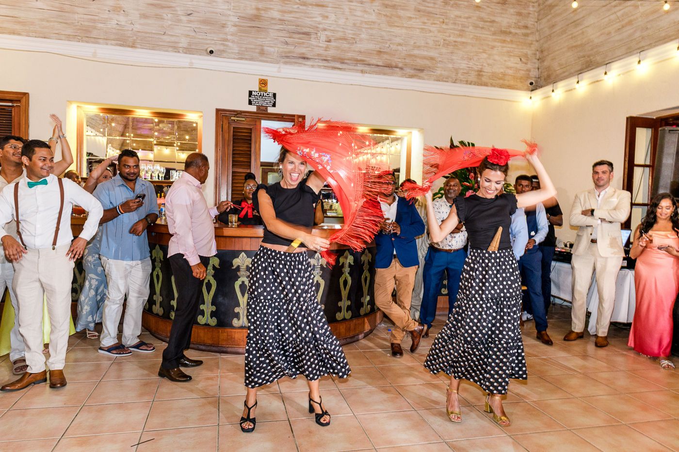 Guests in polka dot dresses dance together during a festive celebration in a rustic venue.