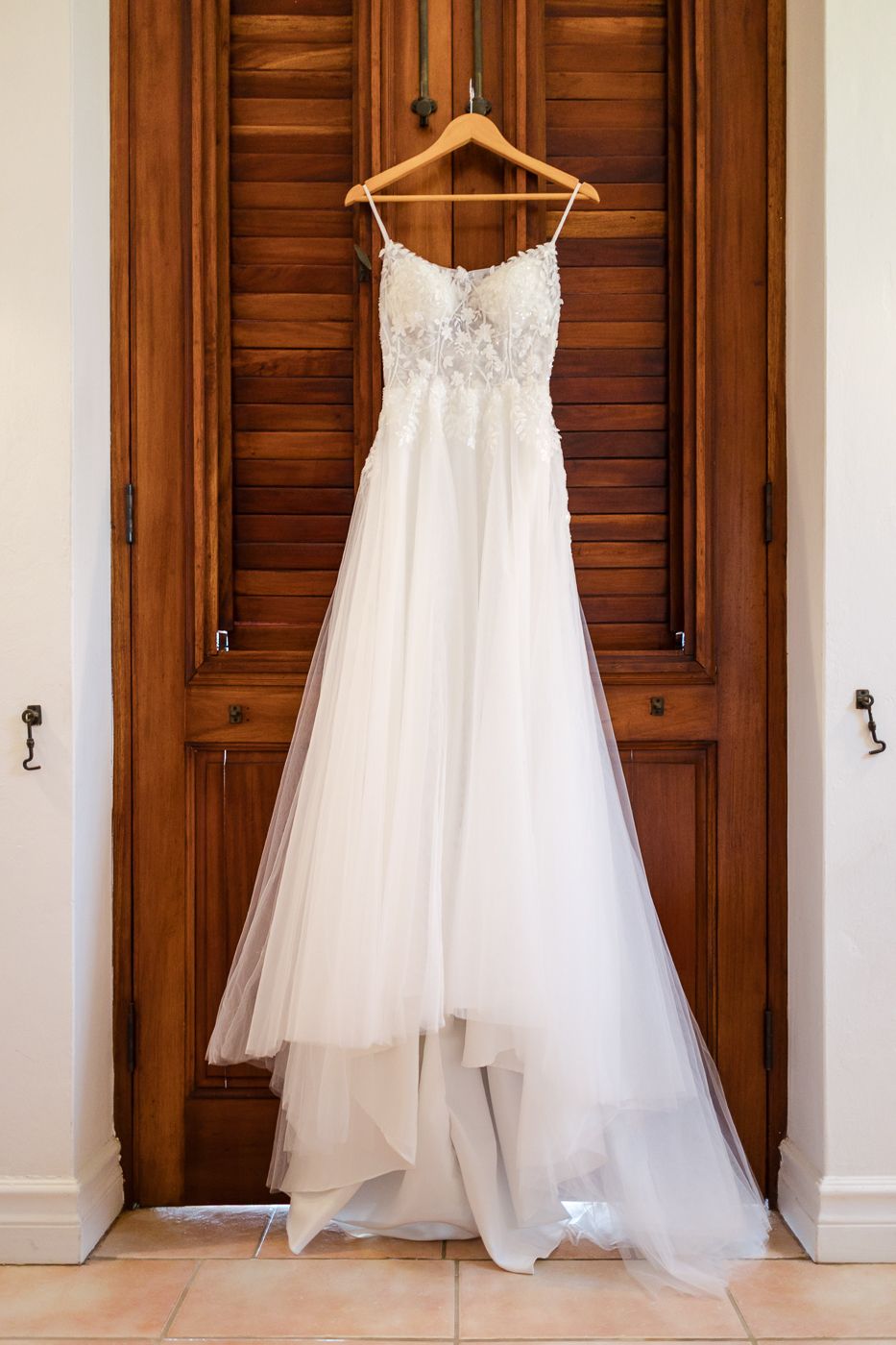 Elegant white beaded spaghetti strap wedding dress hanging on a wooden door before the ceremony.
