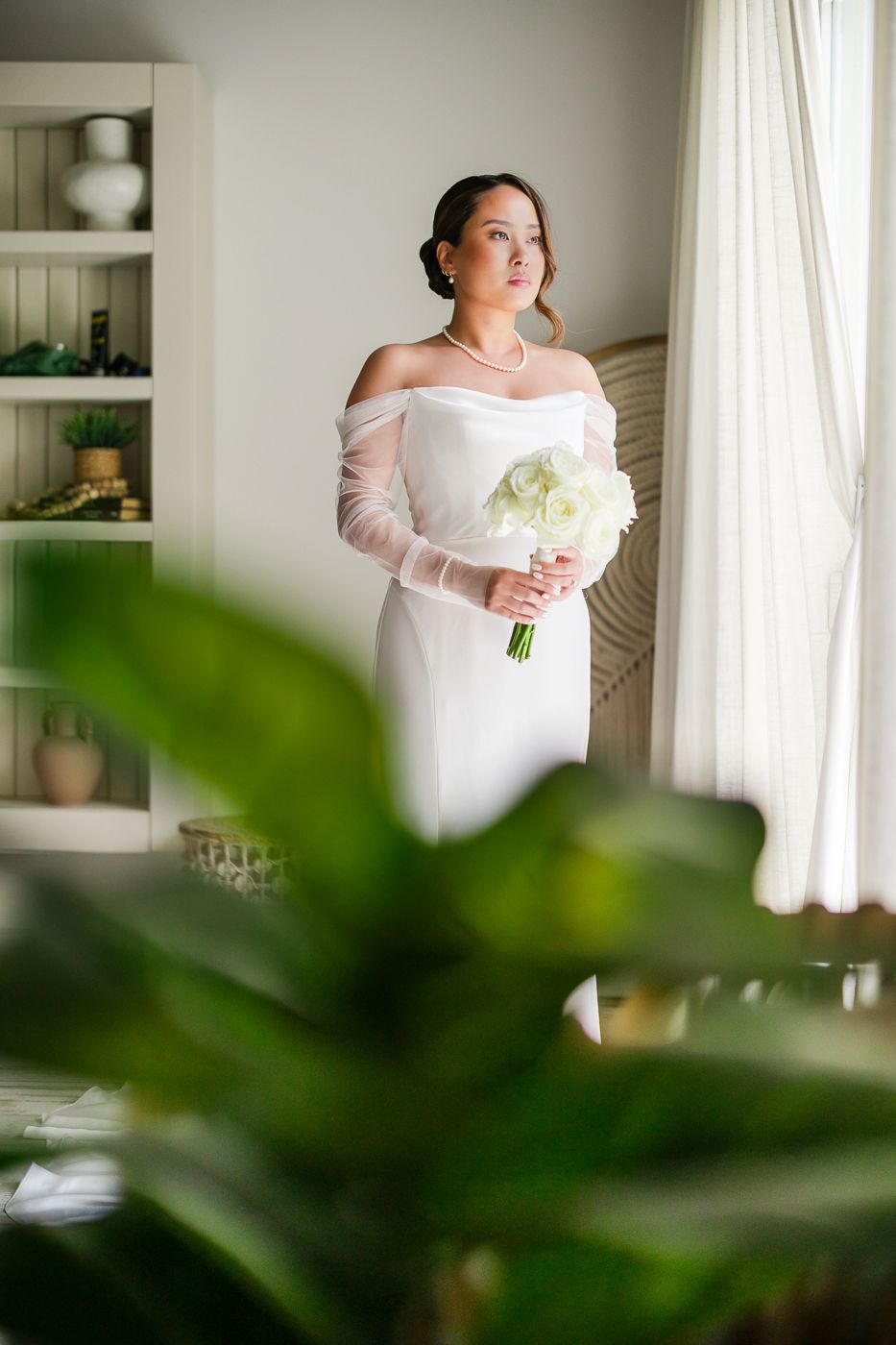 A white wedding dress is showcased in an elegant room with soft natural lighting and built-in shelves.