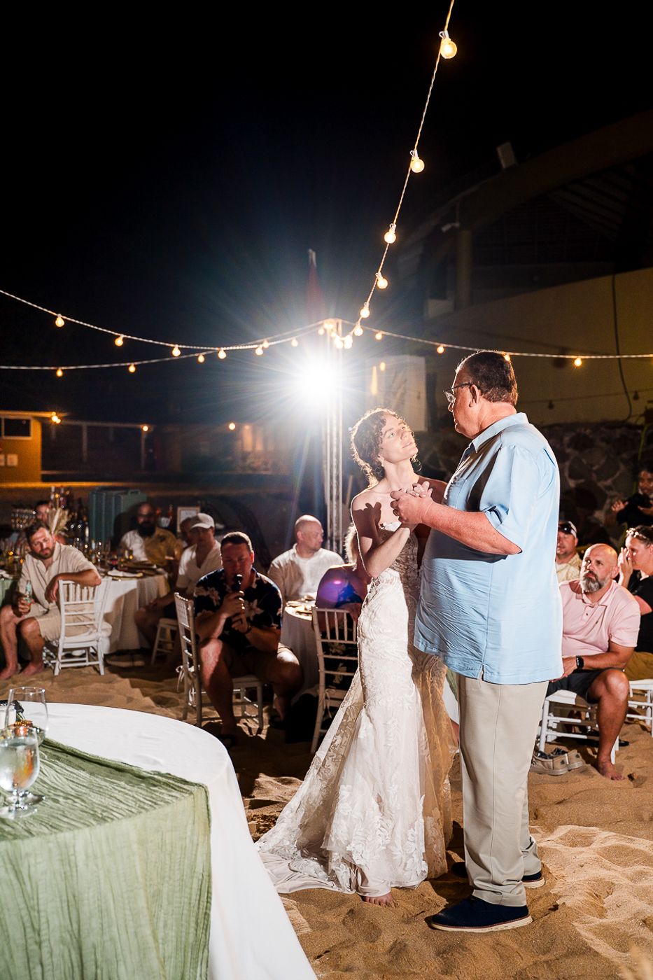 First dance at beachside wedding reception with string lights overhead.