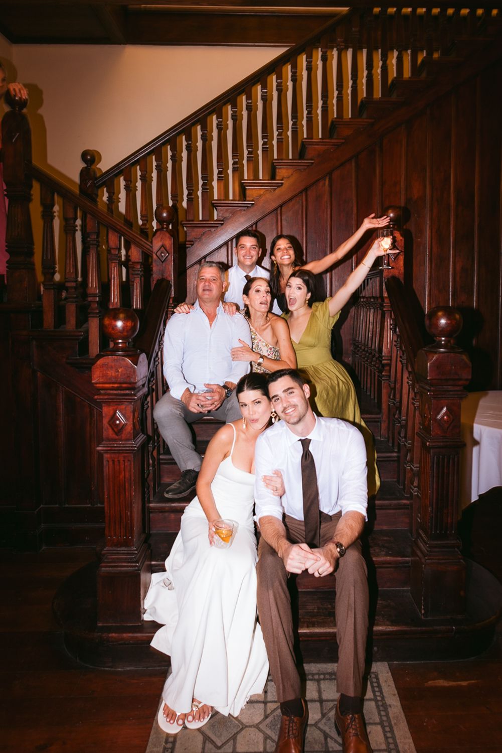 Group of people posing together on an elegant wooden staircase in a dimly lit interior setting.
