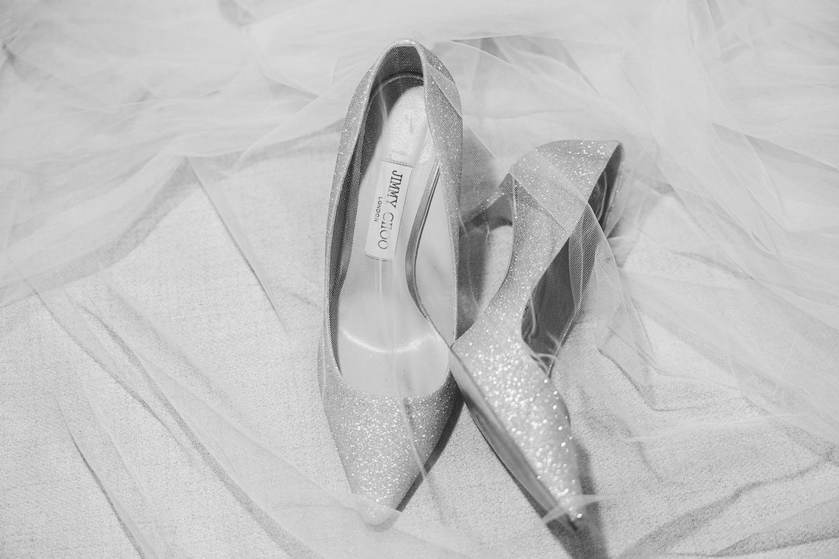 Black and white photo of glittery bridal heels by Jimmy Choo resting on a soft white wedding veil.
