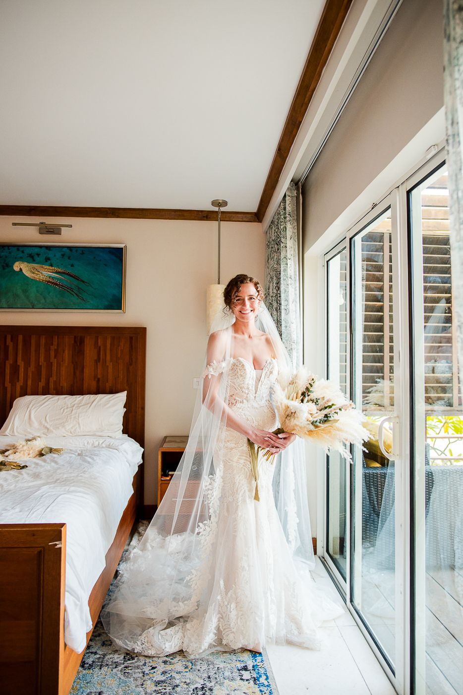A wedding dress with flowing veil photographed in a bright sunlit room with large windows.