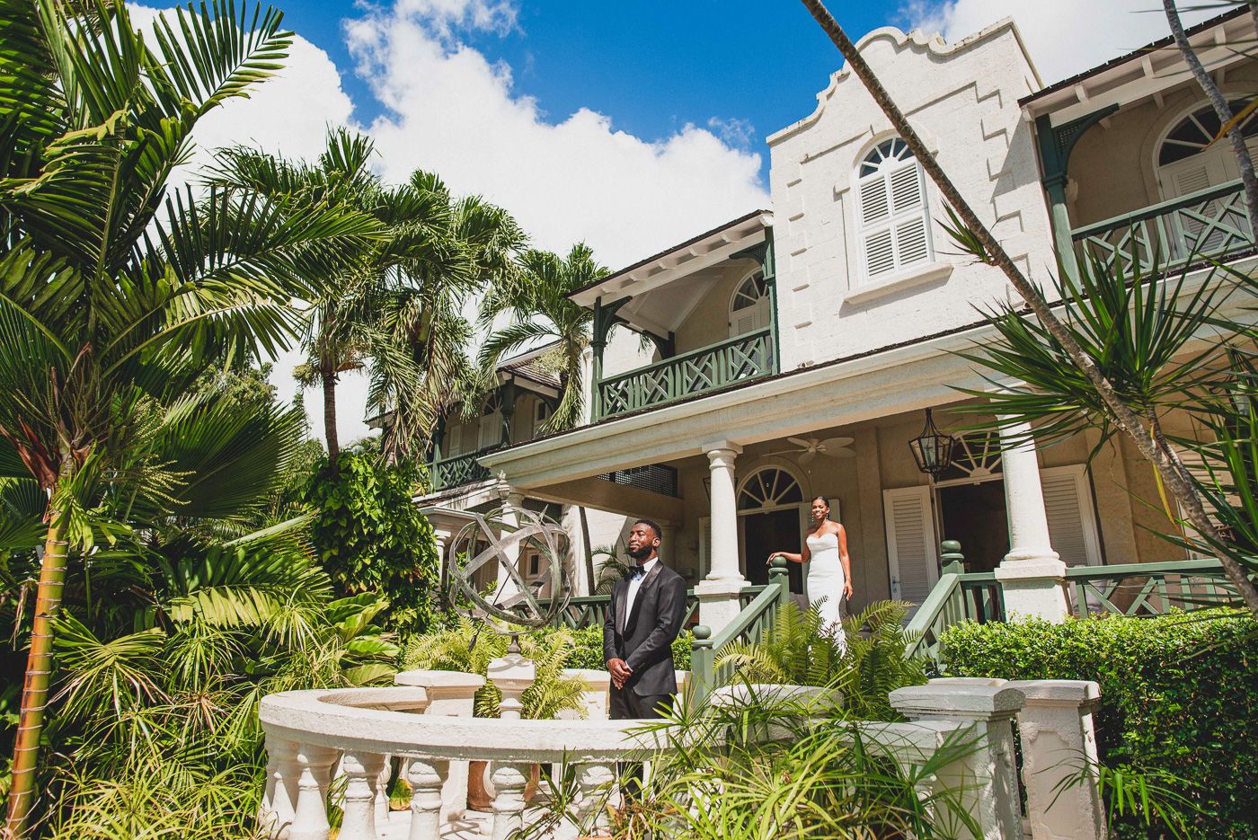 Wedding couple poses on tropical garden terrace with classic white colonial architecture.