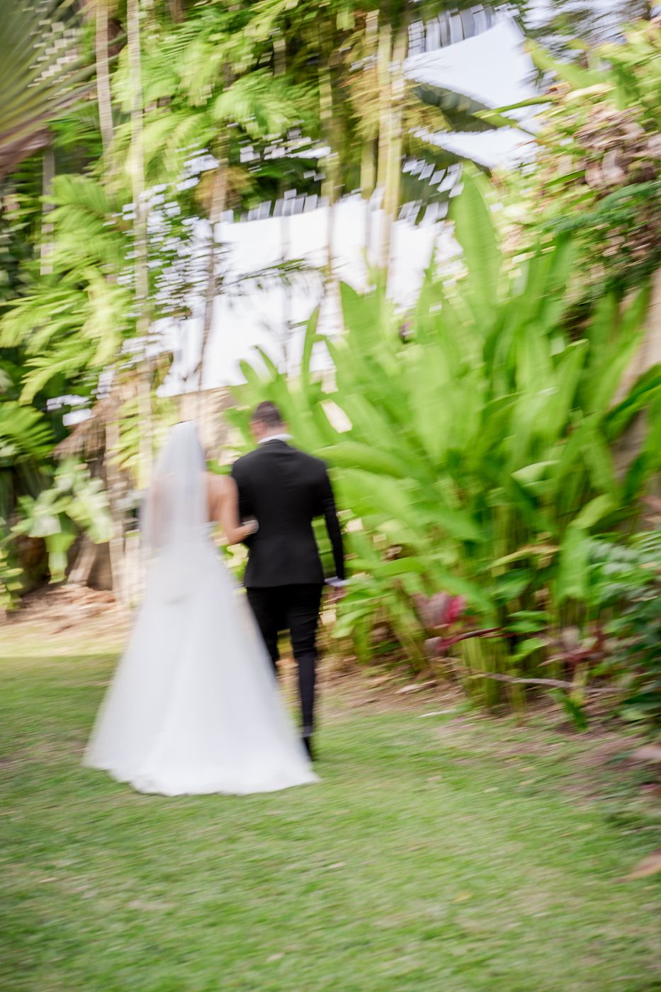 Bride and groom walking hand in hand through a lush tropical garden on their wedding day.