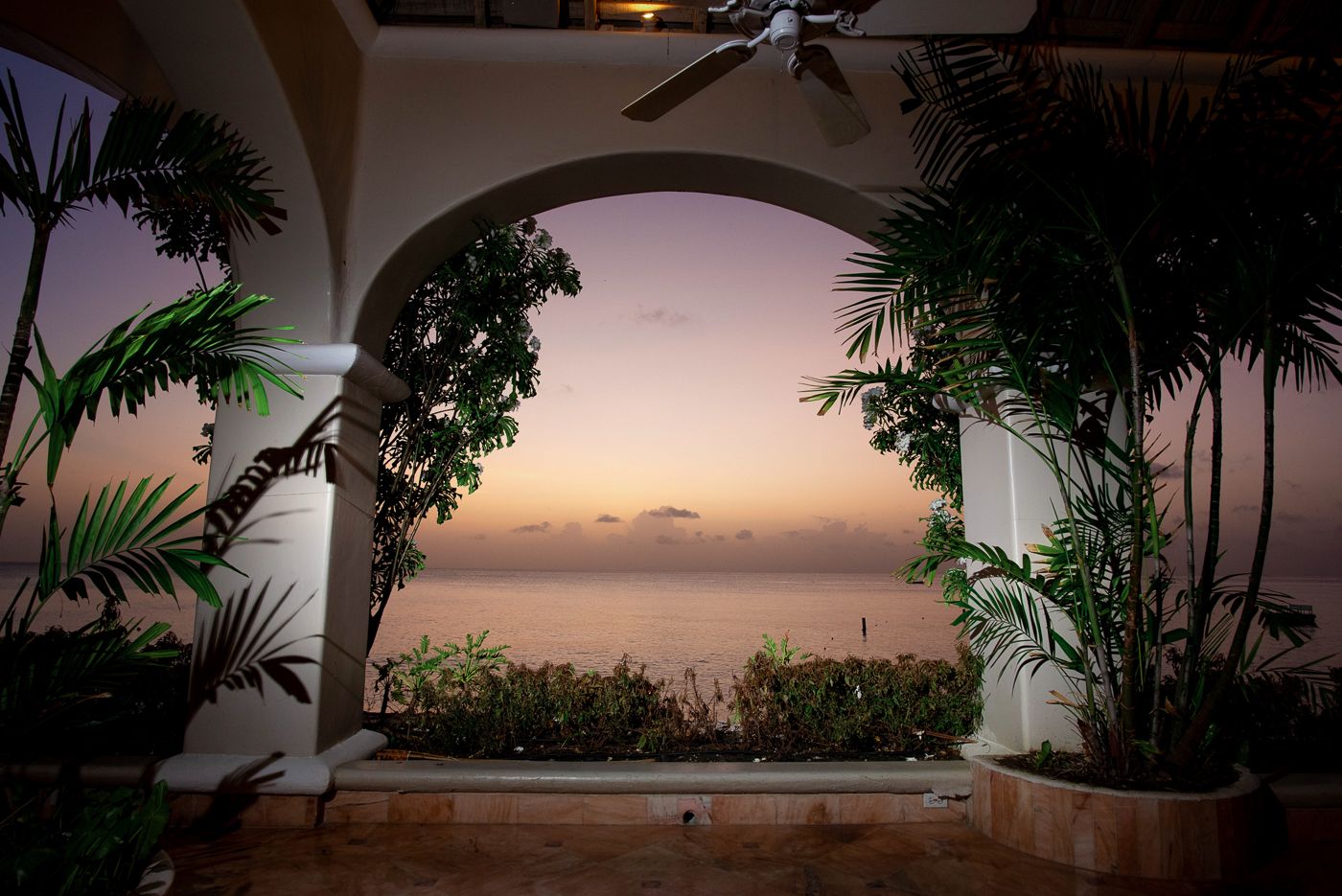 Scenic ocean sunset view framed by white archway and tropical plants.