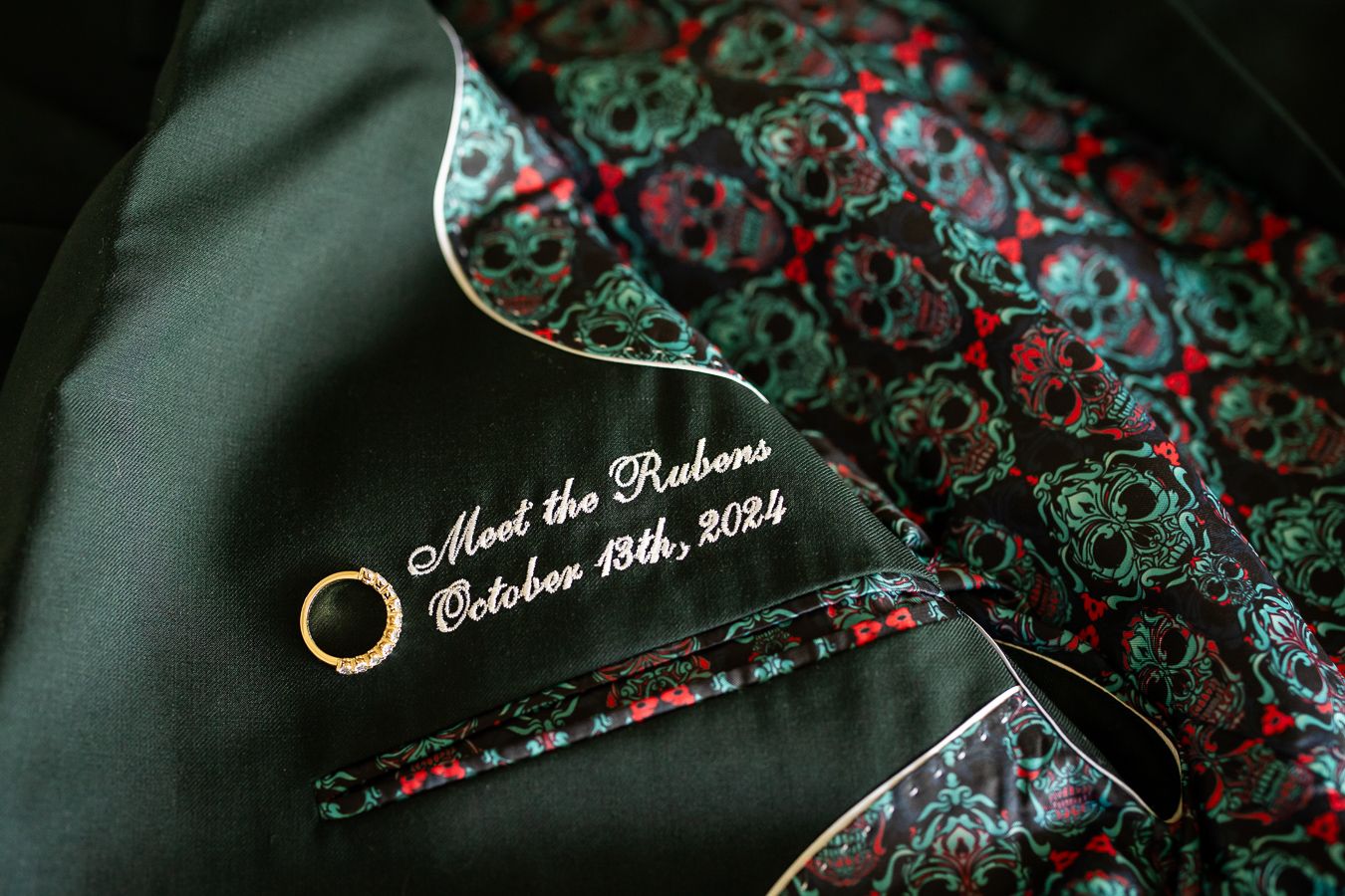 Wedding ring and embroidered date detail on patterned dark fabric.