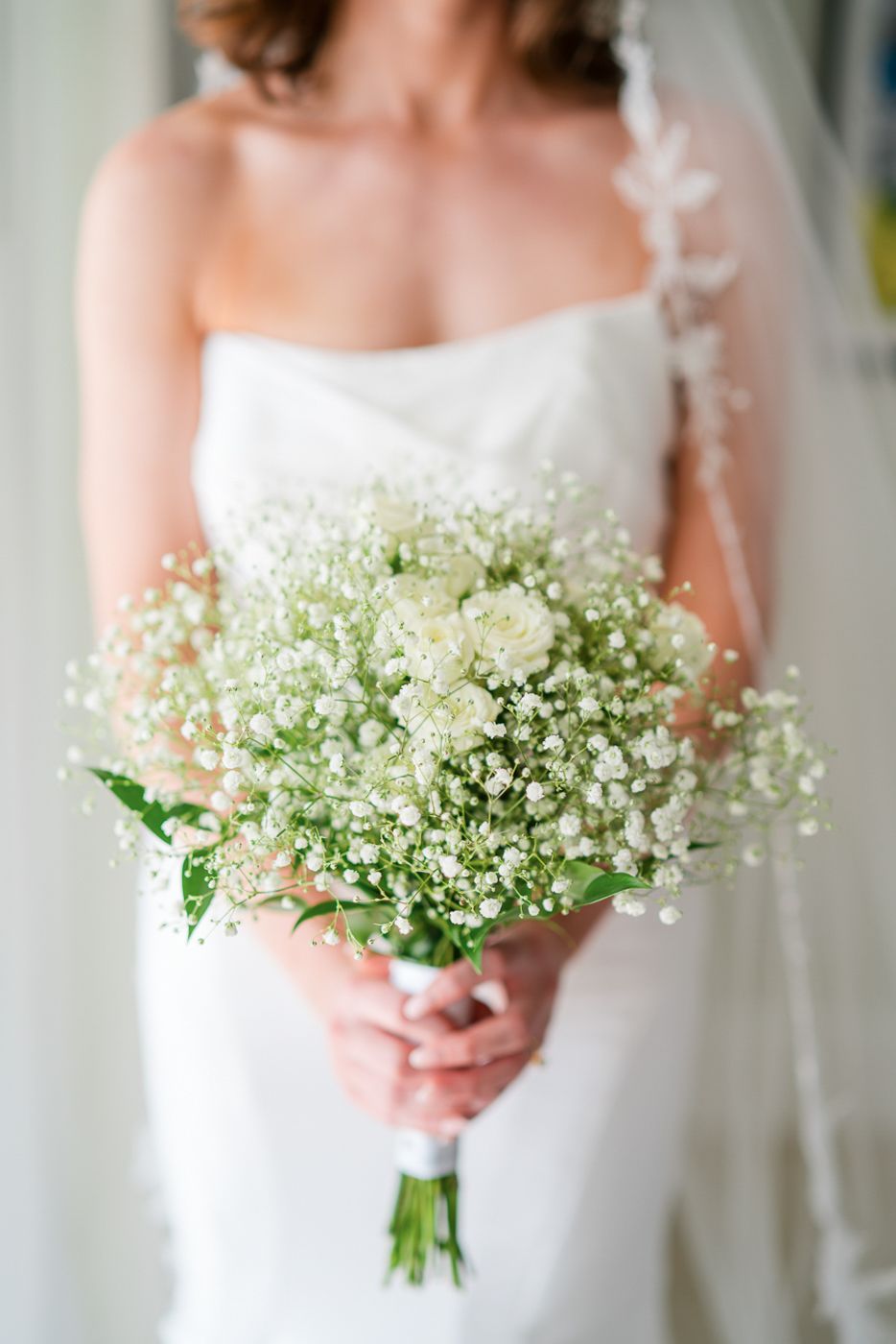 A delicate white bouquet of baby's breath flowers held by a bride in a strapless wedding gown.