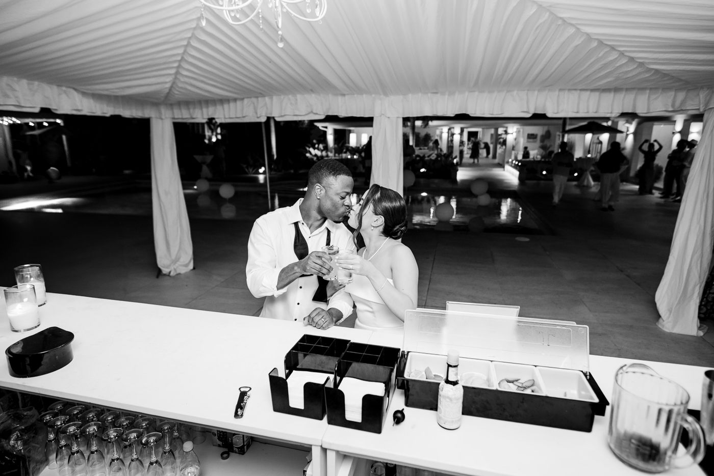 Black and white photo of guests celebrating under a white tent at an outdoor reception.