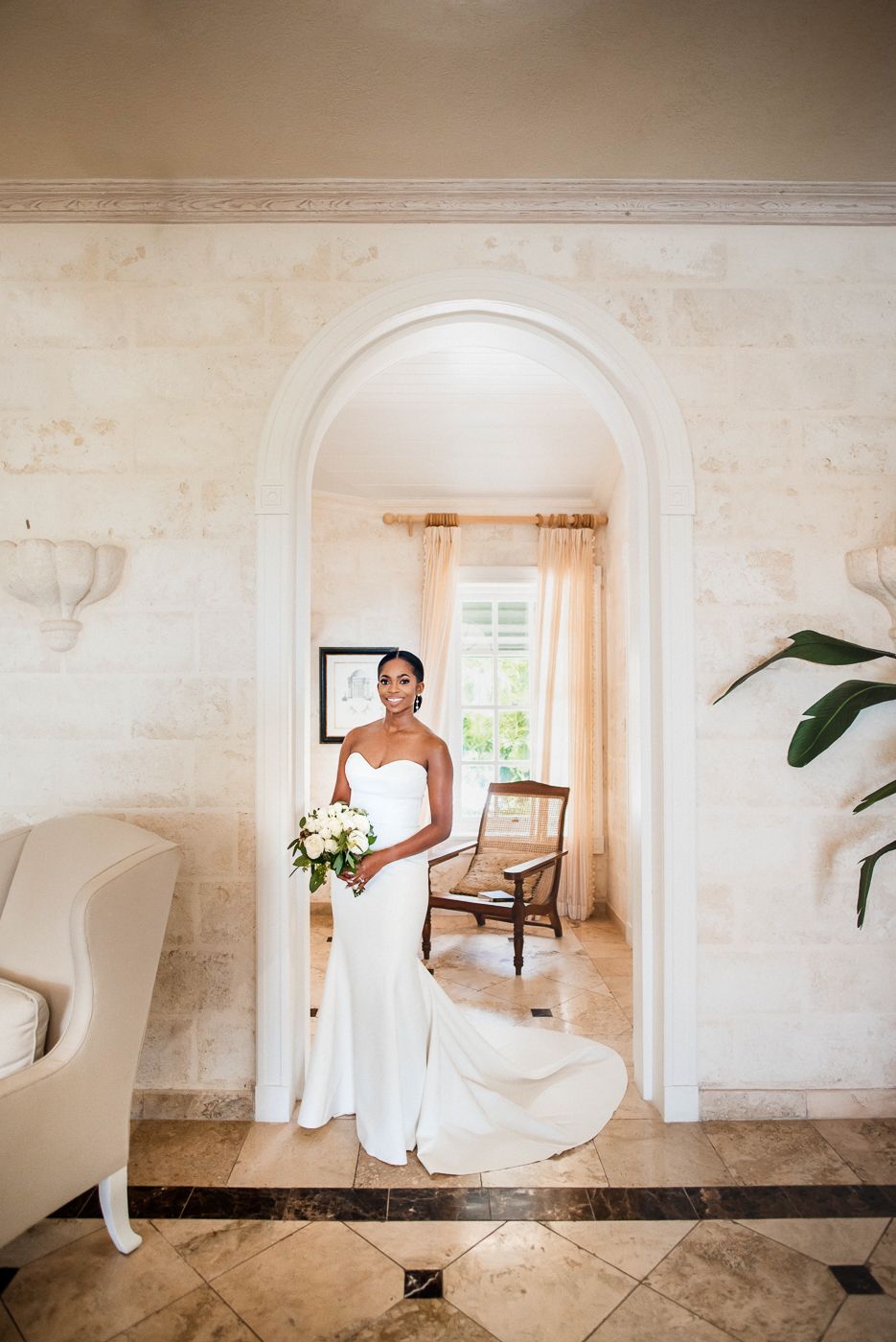 Elegant bridal portrait framed within arched doorway holding white bouquet in classic interior.