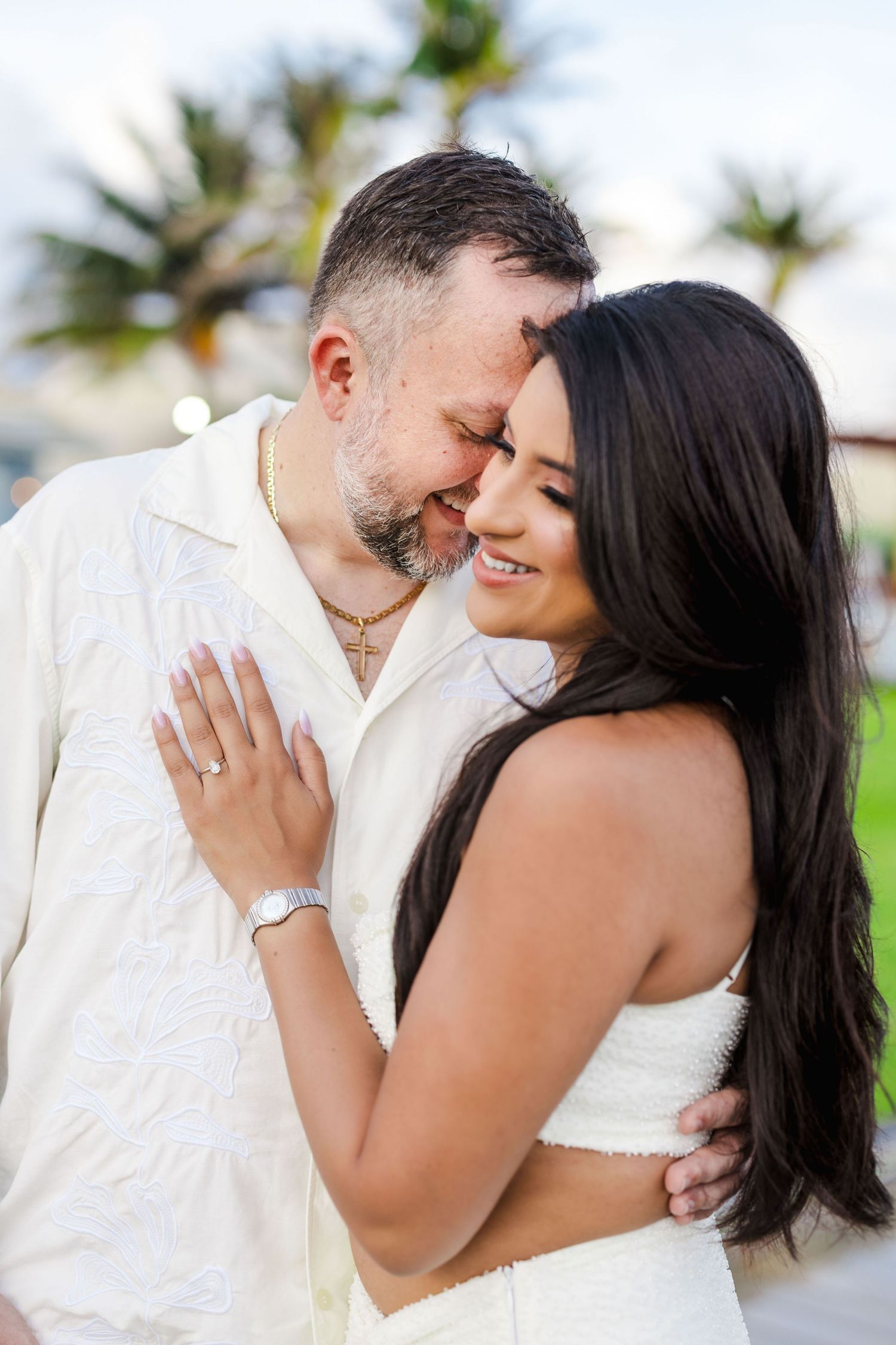 Romantic wedding couple embracing outdoors with palm trees in the background.