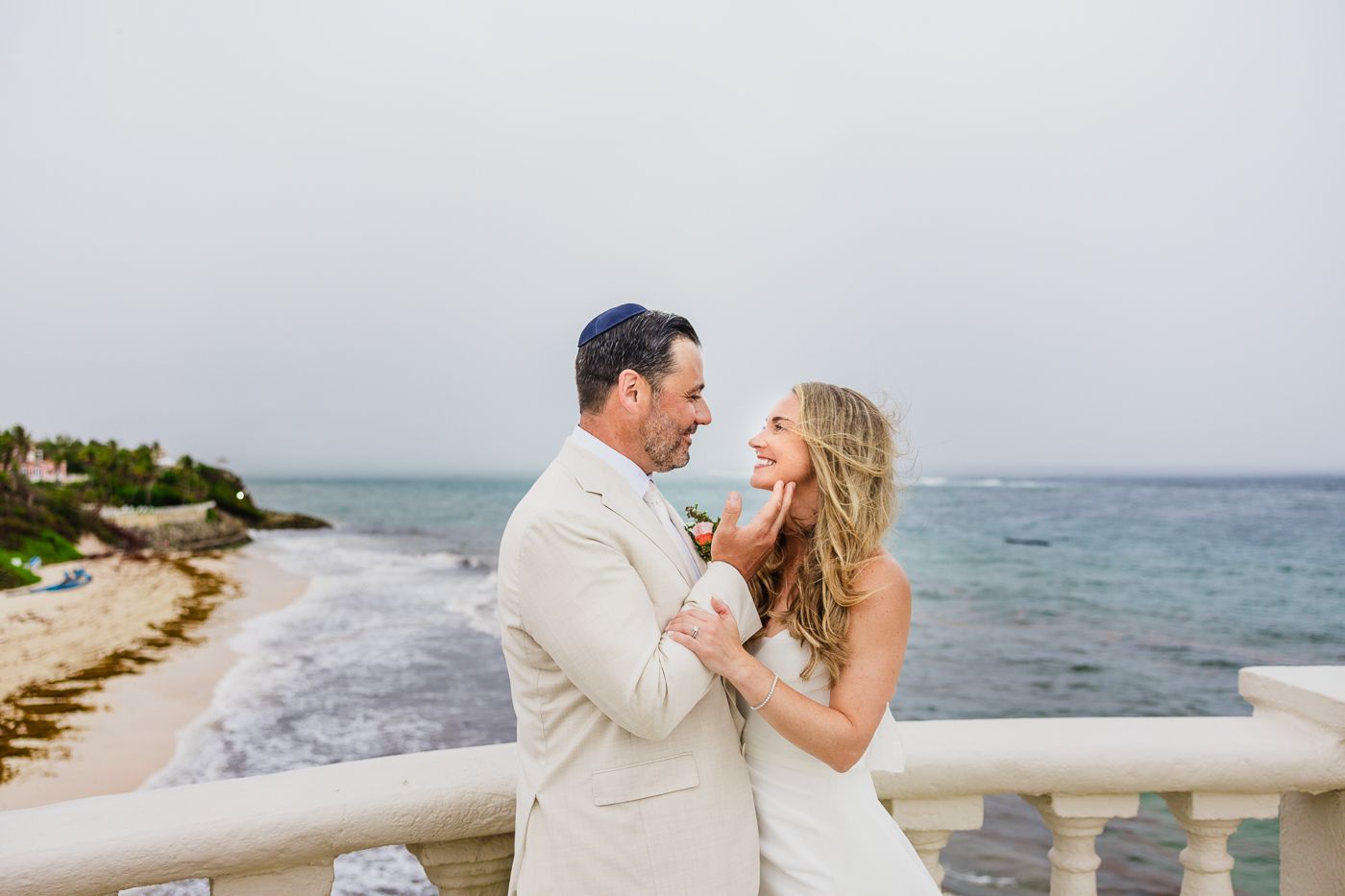 Couple sharing a romantic moment in wedding attire on a seaside balcony with ocean views.