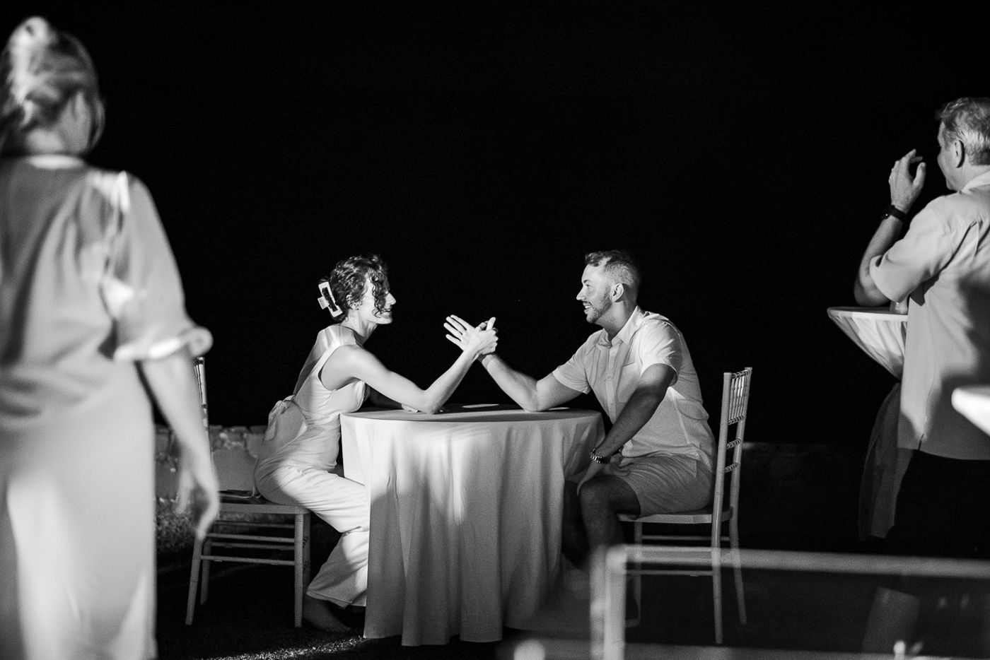 Black and white photo of two people arm wrestling at a candlelit table.