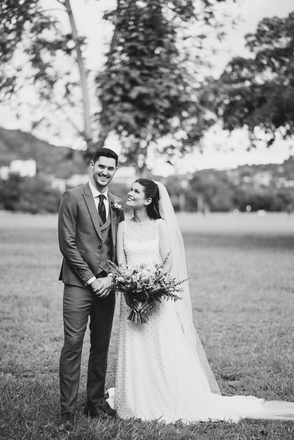 A black and white wedding photo series showing a couple outdoors in a grassy field with trees in the background.