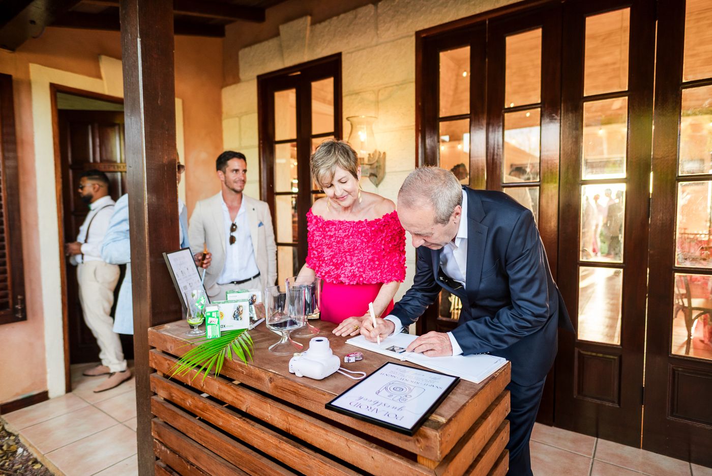Wedding guests signing the guest book at a wooden registration table.