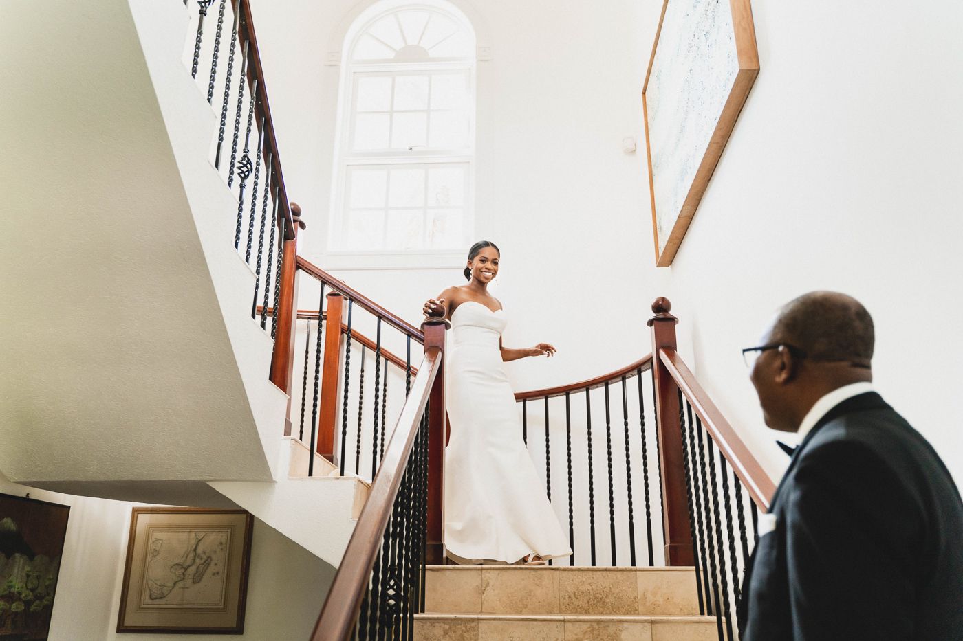 Dramatic wedding photo taken on an elegant staircase with natural lighting streaming through arched window.