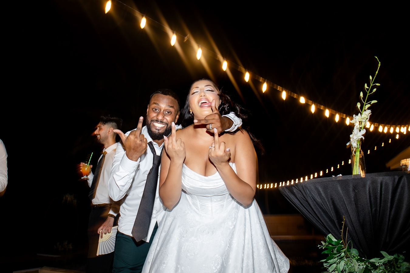 Wedding couple and guests dancing joyfully under string lights during an outdoor evening reception.