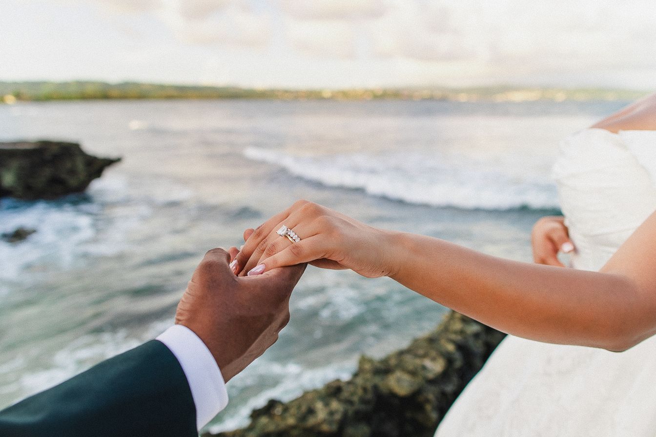 Close up of hands clasping together against a blurred ocean background during a romantic beach moment.