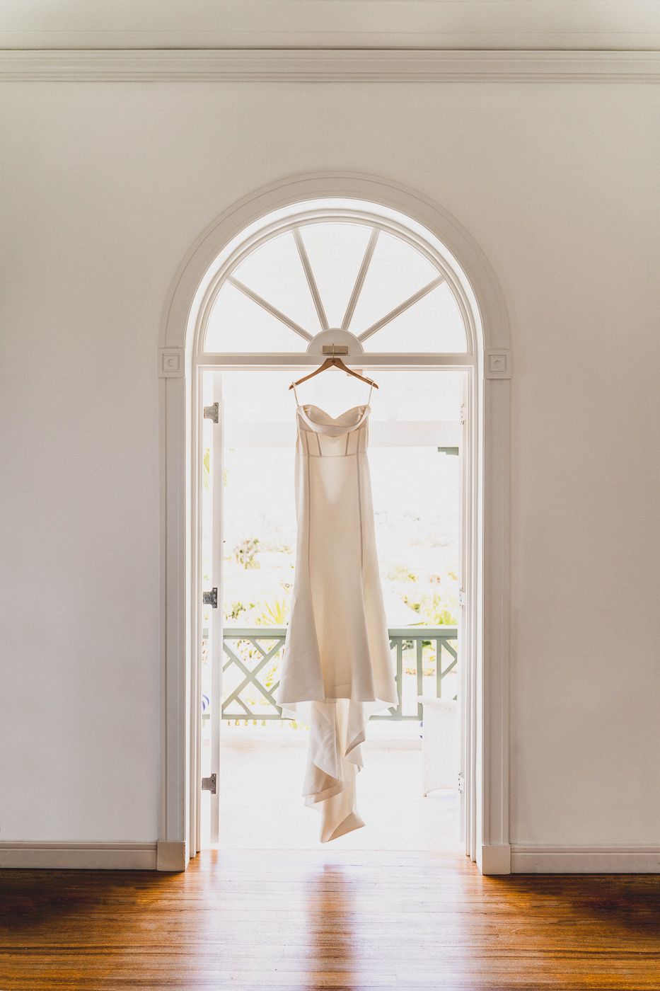Elegant champagne-colored wedding dress hanging in arched doorway with natural light.