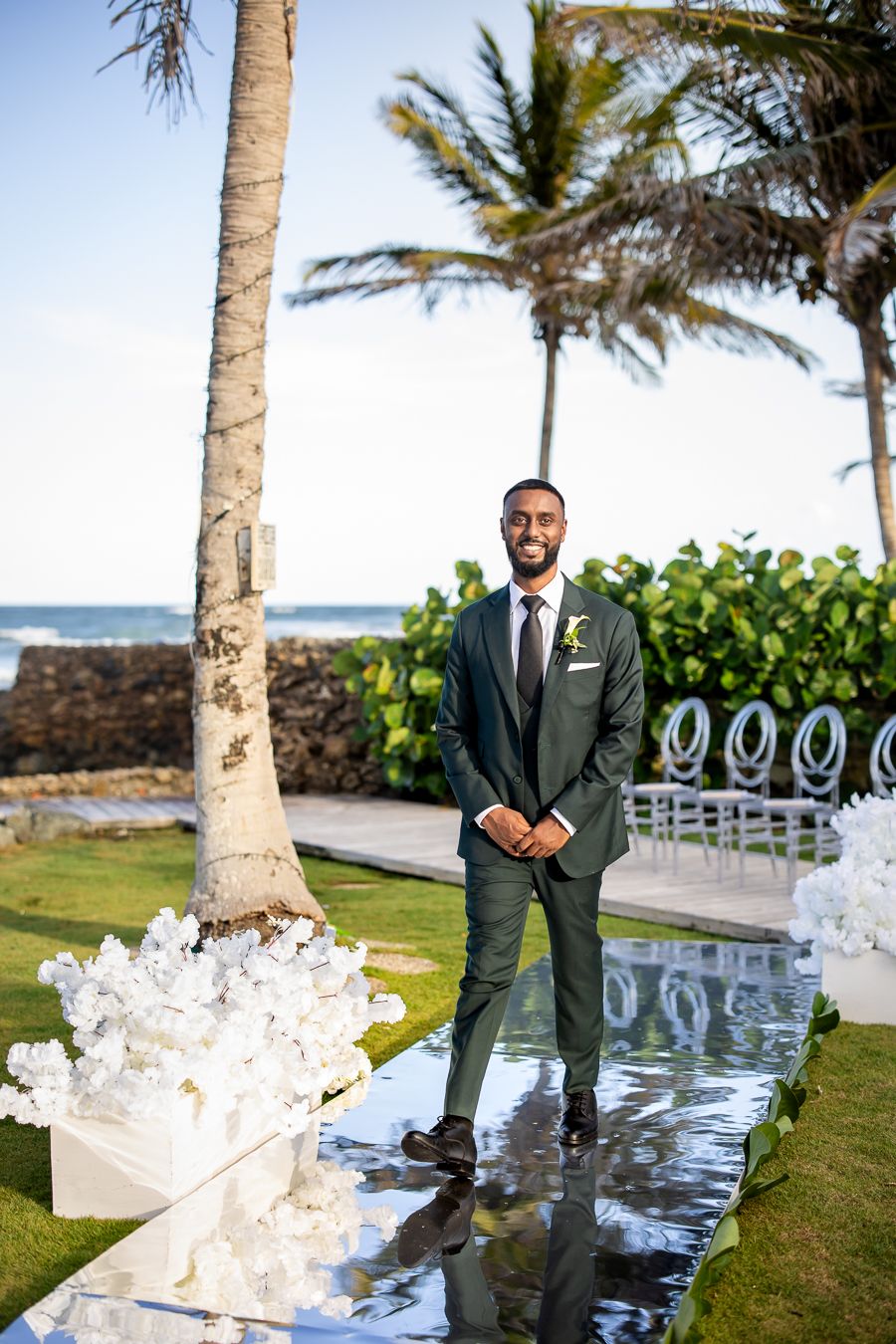 Outdoor wedding venue decorated with white floral arrangements along palm tree-lined aisle.
