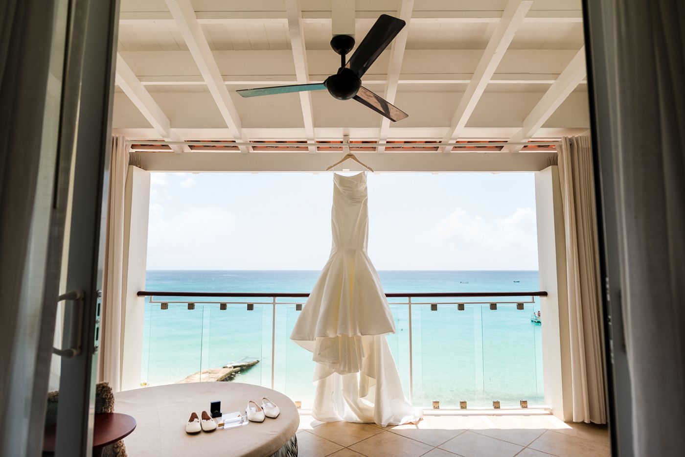 Ocean view through white-framed windows with wedding dress hanging in silhouette.