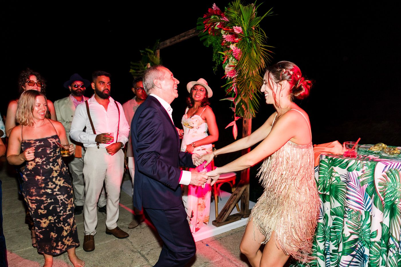 Tropical-themed party with guests in floral prints dancing under evening lighting.
