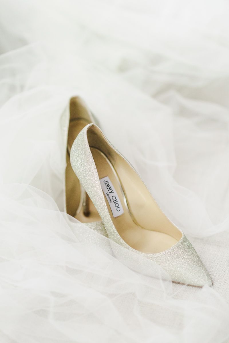 Elegant silver glitter Jimmy Choo pointed-toe pump rests on white tulle fabric.