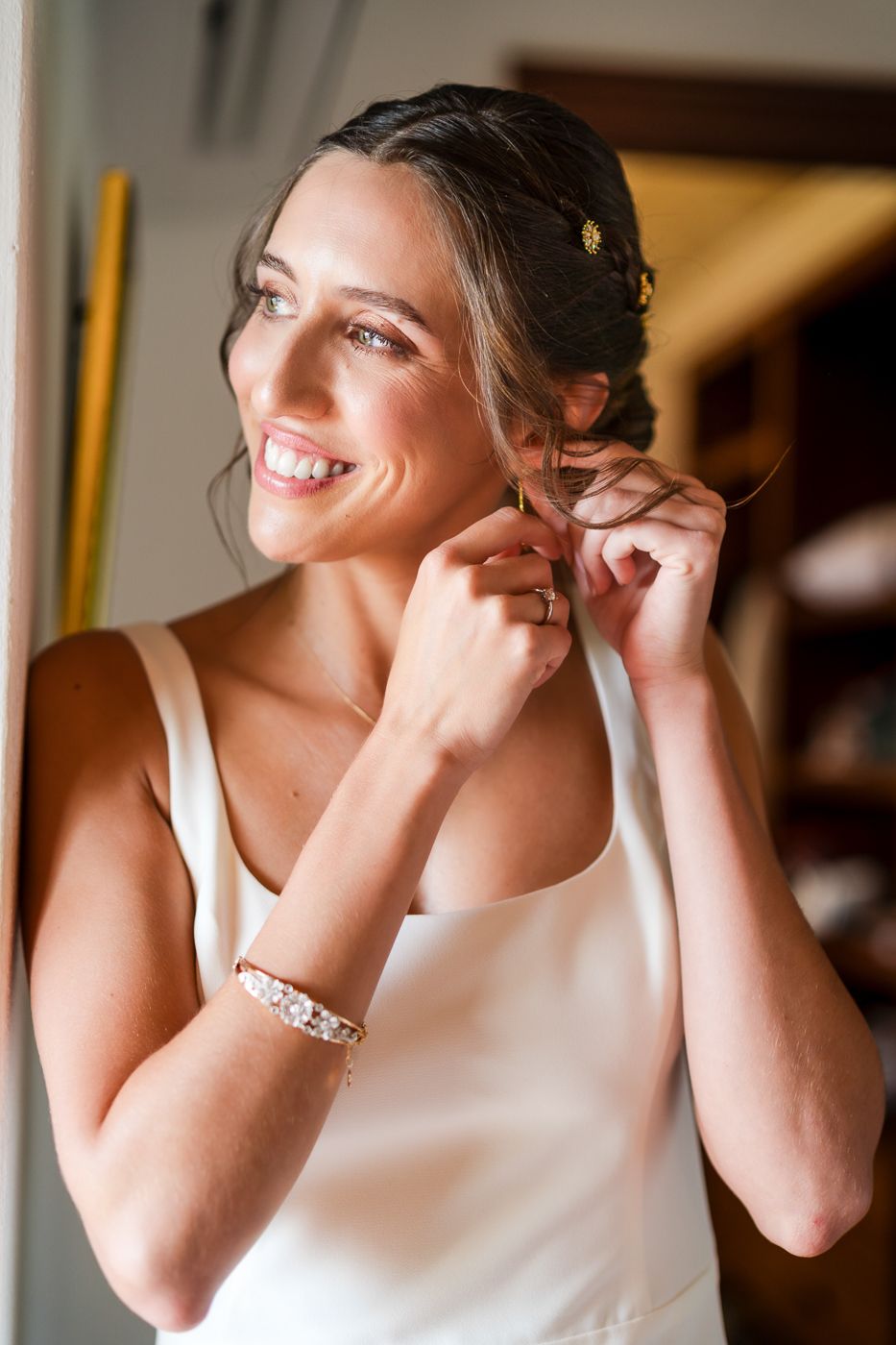 Close-up sequence of someone putting on earrings while wearing a white sleeveless dress.