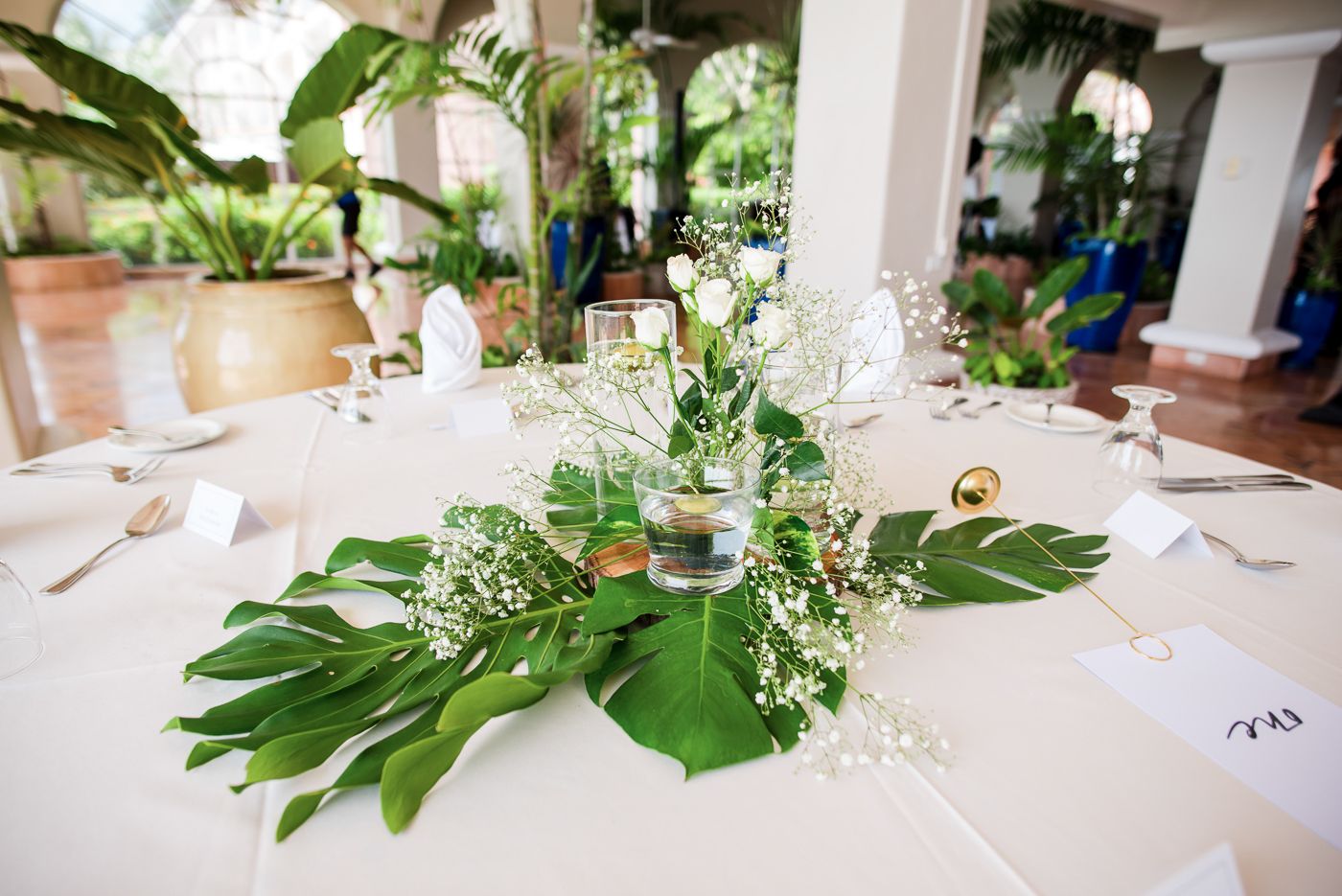 White wedding table decorated with lush green tropical leaves and delicate floral centerpieces.