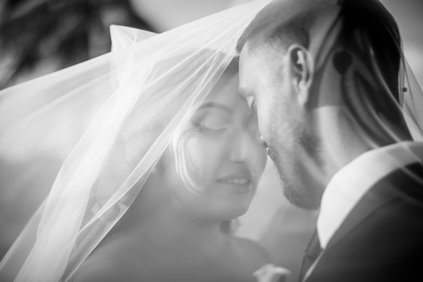 Black and white close-up of newlyweds sharing an intimate moment under a delicate veil.