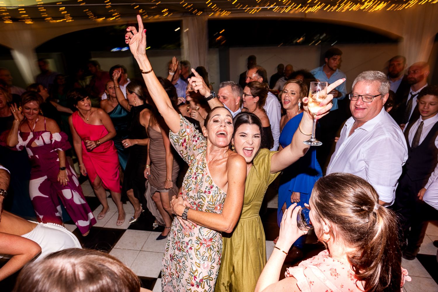 Happy guests dance and celebrate together on the illuminated dance floor at an evening wedding reception.