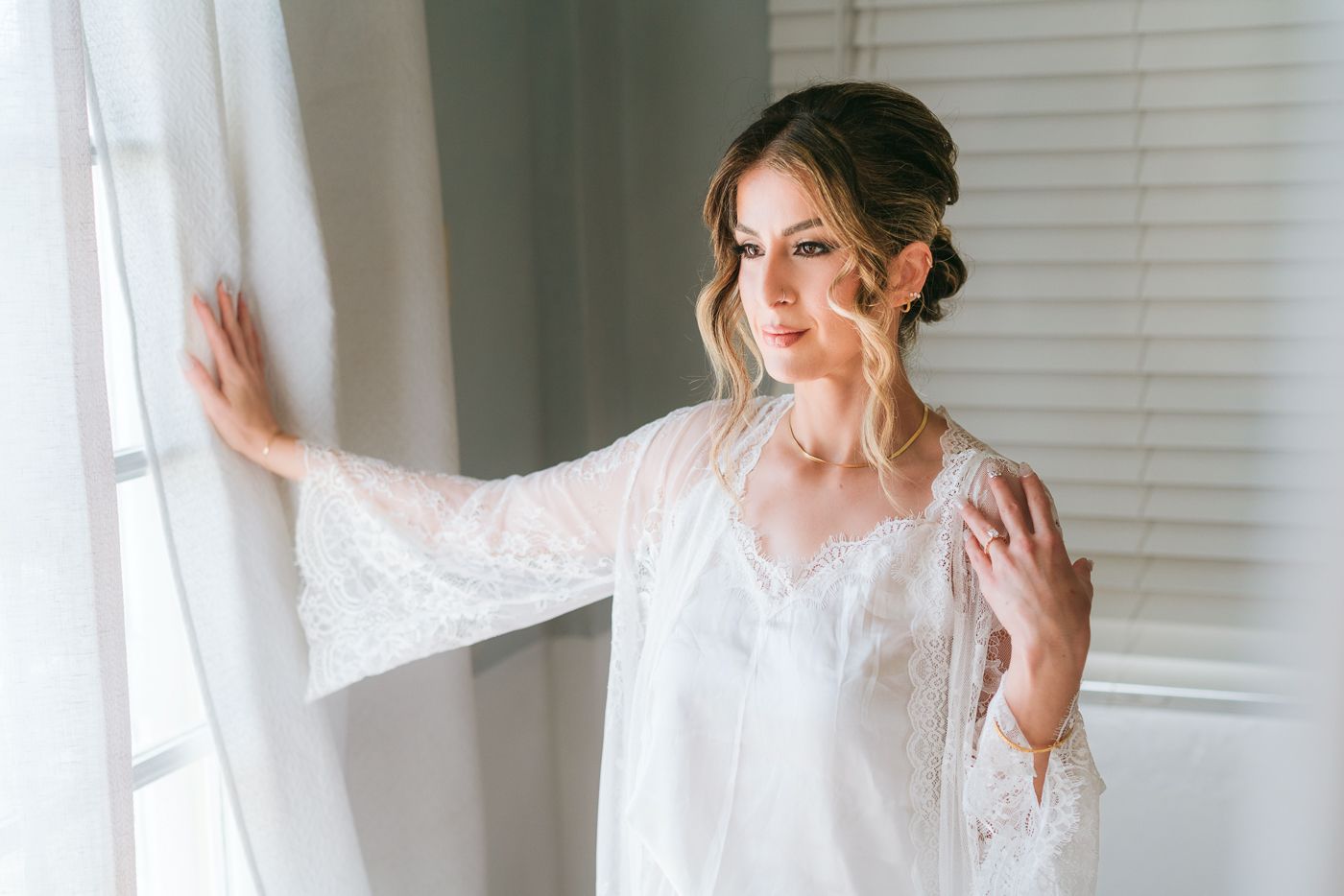 Ethereal bridal boudoir photo with white lace robe near window light.