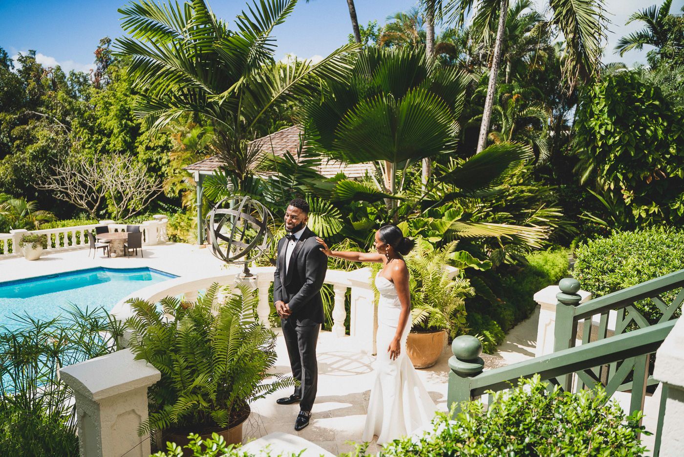 Elegant couple descending outdoor stairs surrounded by tropical landscaping and pool area.