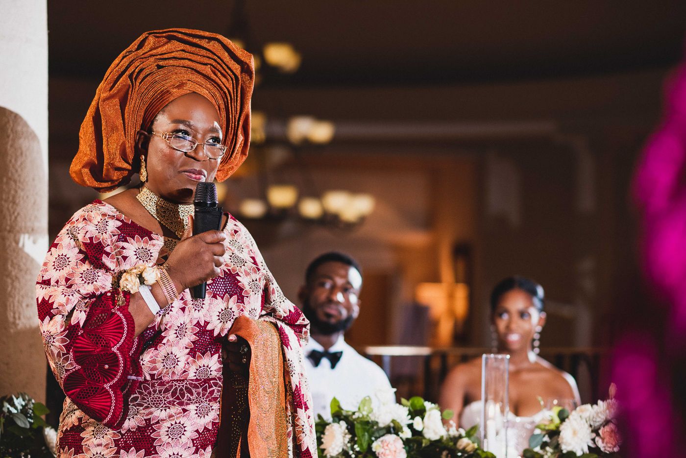 Wedding reception speeches being given at an elegant venue with floral centerpieces and mood lighting.