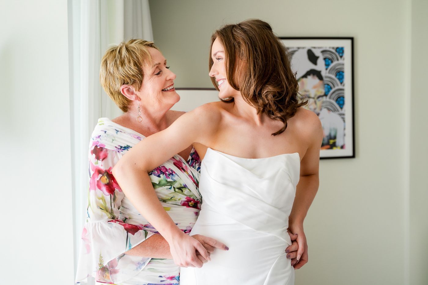 Two women share a joyful moment during wedding preparations in a bright interior setting.