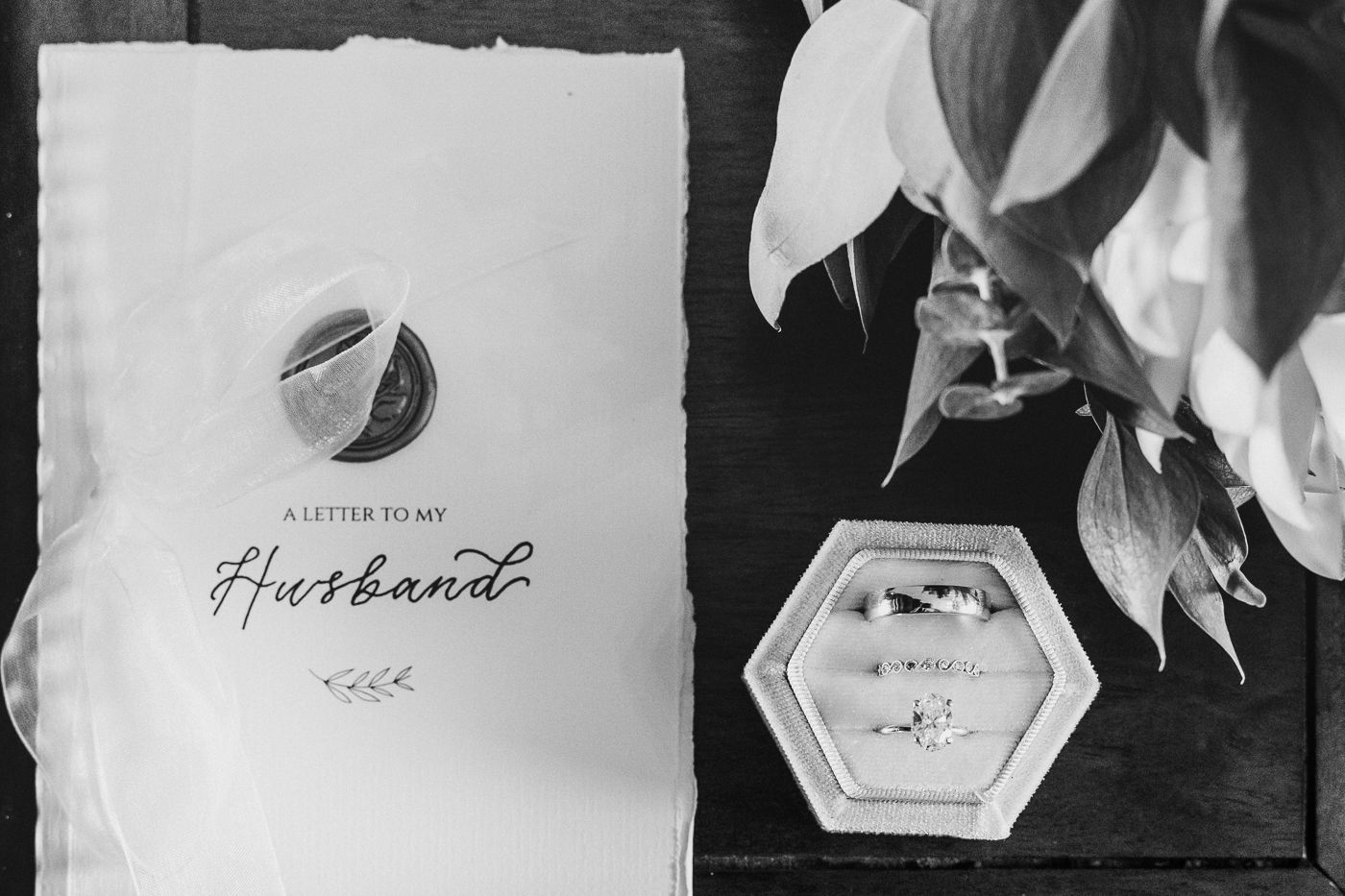 Black and white flat lay of a letter to my husband card with wedding rings in a hexagonal box.