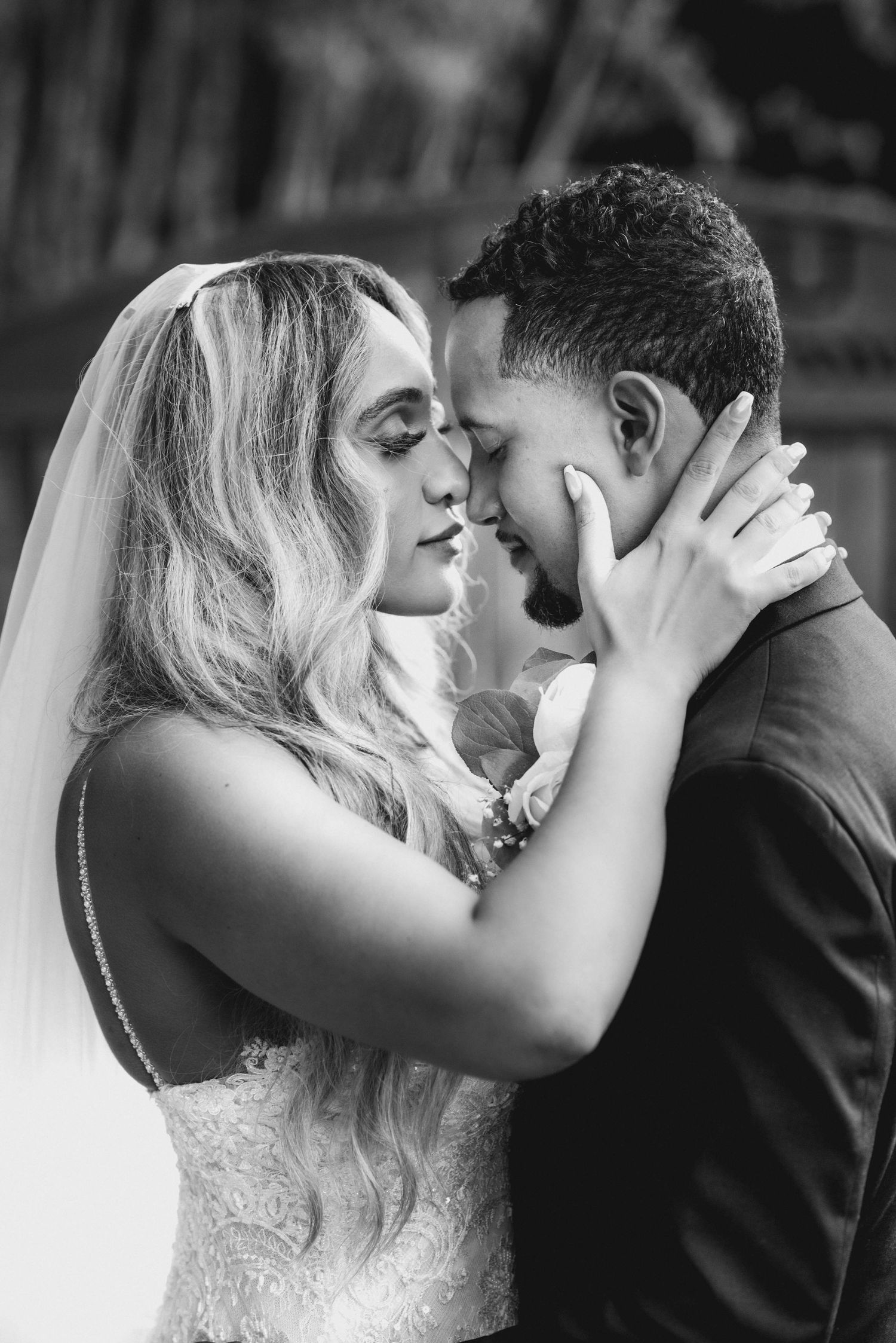 Black and white photo of a bride and groom sharing an intimate moment, foreheads touching, on their wedding day.